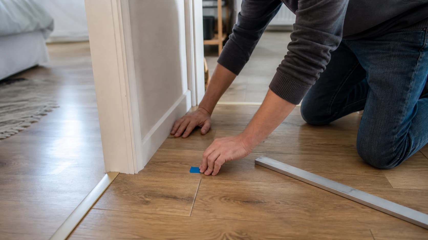 Proprietar care marchează punctul unde scârțâie parchetul laminat lângă un prag și verifică planeitatea
